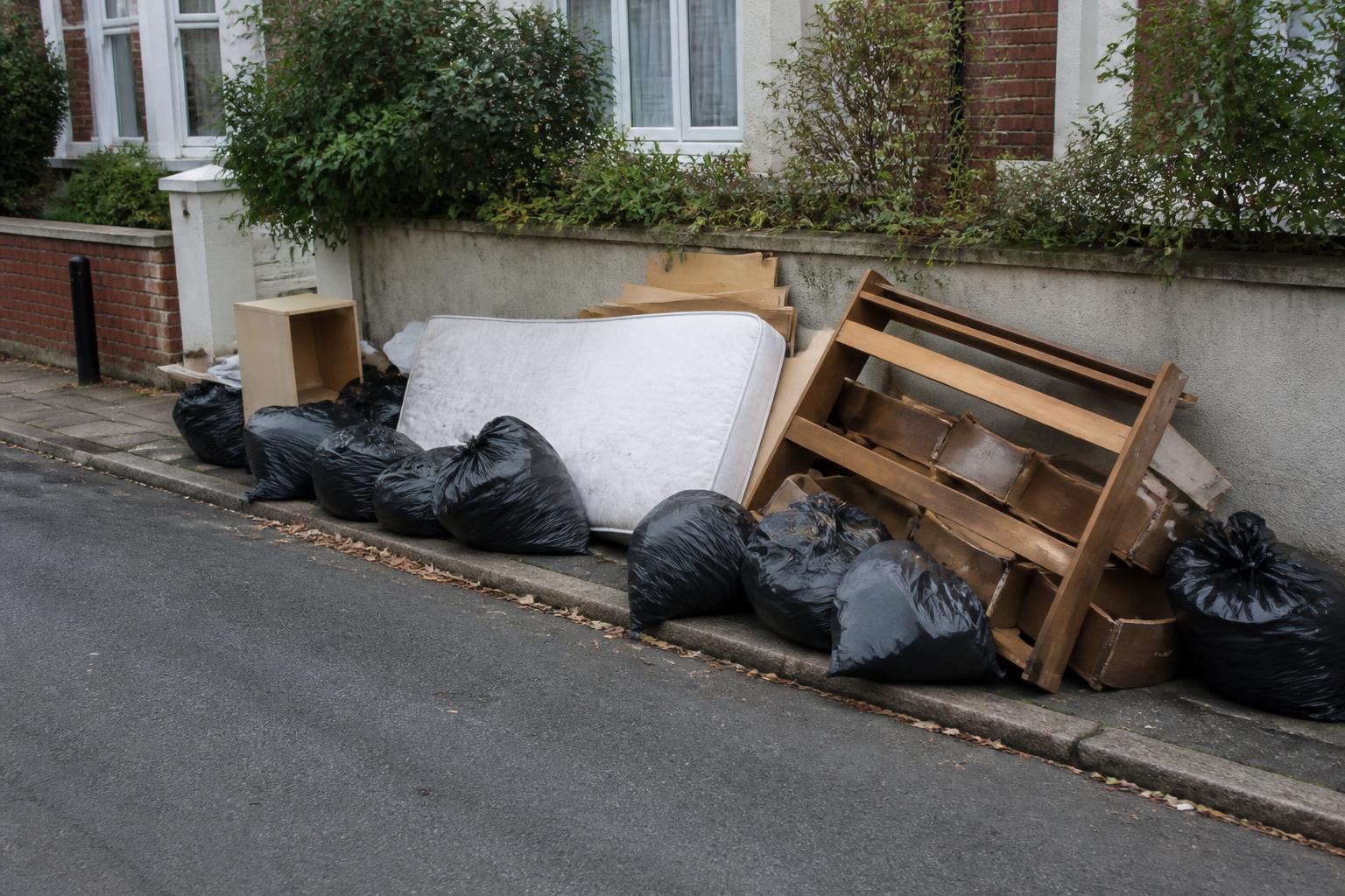 Fly-tipped bin bags, mattress and broken furniture cleared from a UK kerbside